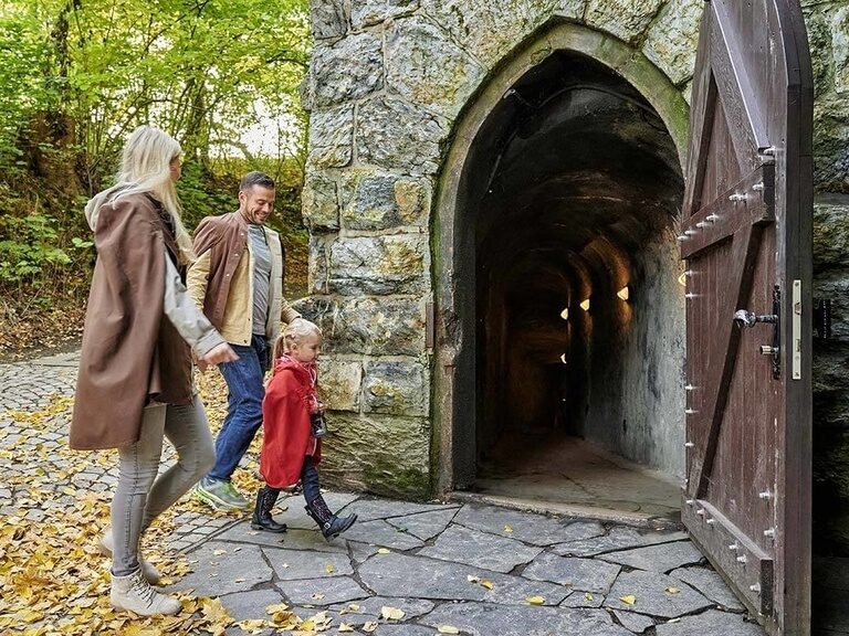 Familie spaziert zum Grotteneingang bei Hotel Oberhof, umgeben von Herbstblättern.