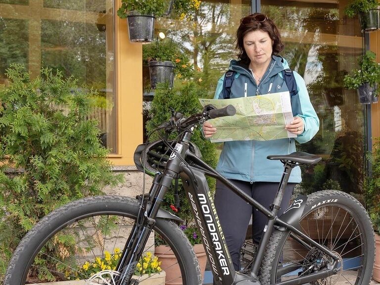 Eine Frau steht mit einem E-Bike vor dem Schlossberghotel und studiert eine Karte.