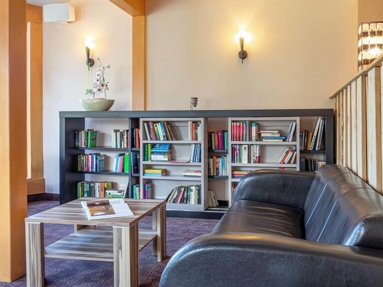 Ein gemütliches Ledersofa samt Couch-Tisch steht vor einem gut gefüllten Bücherregal.