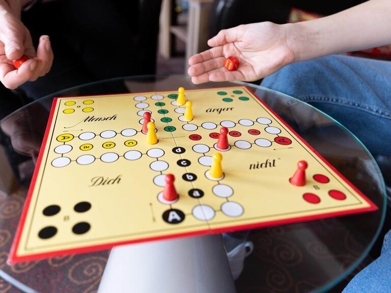 Nahaufnahme eines Mensch-ärgere-dich-nicht-Spiels, bei dem gerade gewürfelt wird.