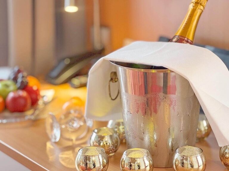 Gekühlter Champagner, Obst und Teelichter auf dem Tisch im Hotelzimmer.