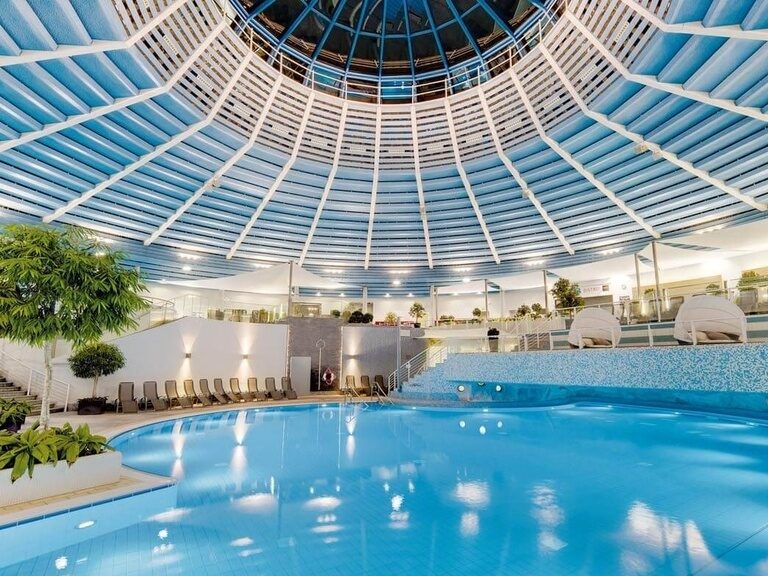 Großes Becken mit Wasserfall-Grotte und viele Ruheliegen ringsherum.