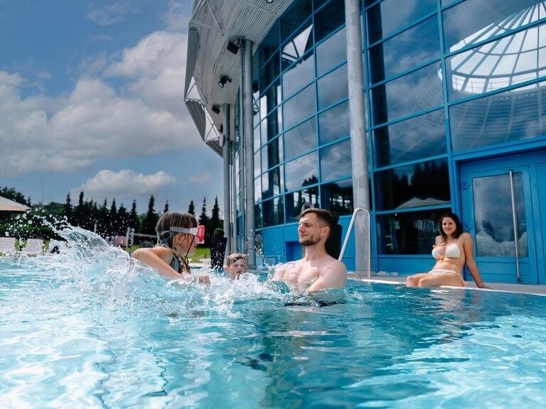 Eine Familie plantscht im Sommer im Außenbecken.