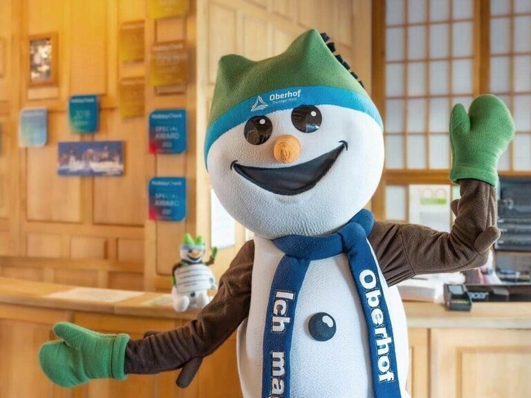Oberhofs beliebtes Maskottchen "Schneemann Flocke" winkt an der Hotel-Rezeption fröhlich in die Kamera.
