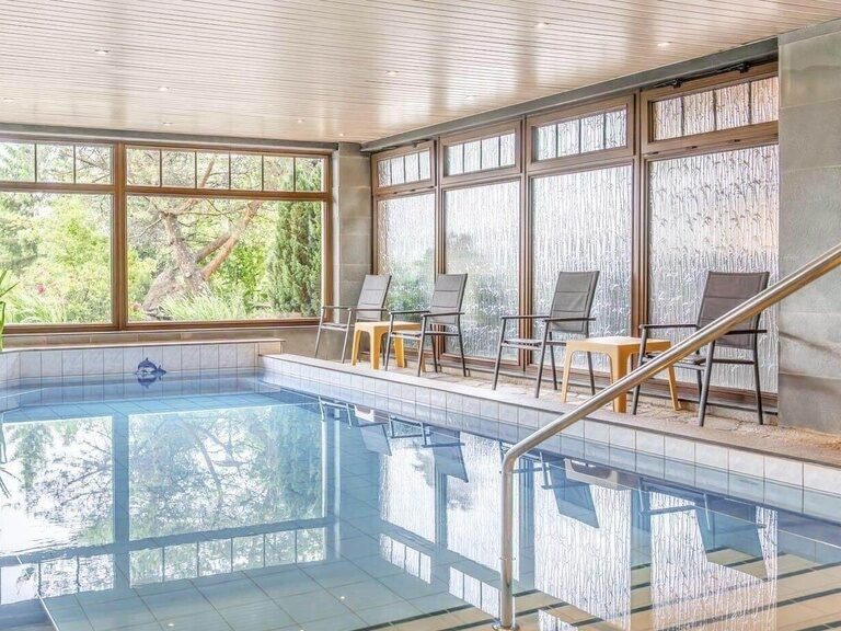 Chairs and tables are placed next to the hotel's indoor pool, which shimmers a beautiful blue.