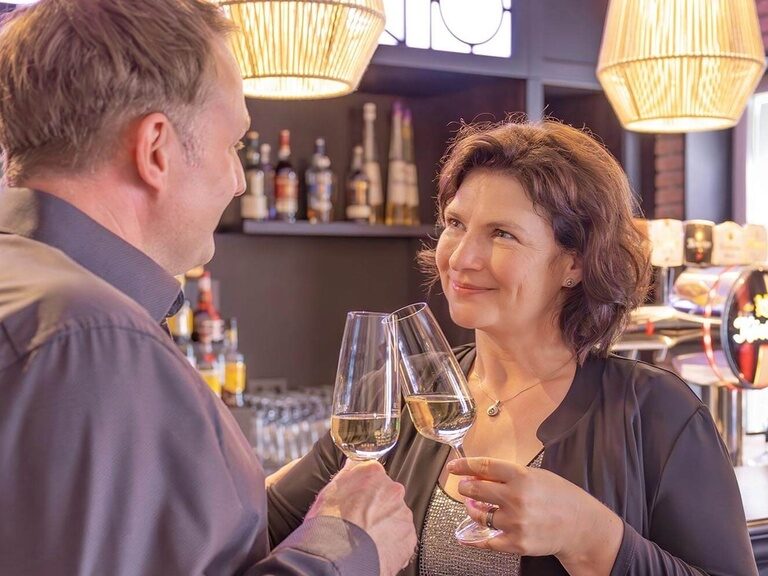 Ein Paar stößt mit Sekt an der Hotelbar an und schaut sich verträumt in die Augen.