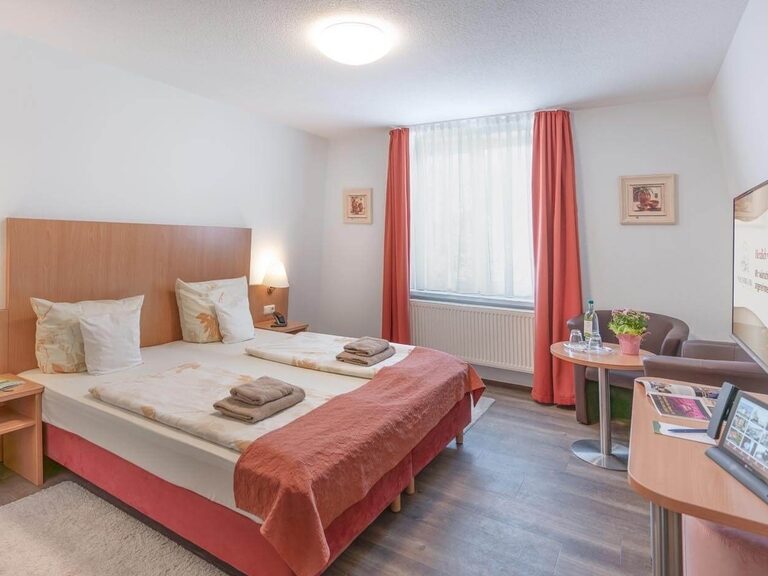 Blick in eines der Economy Zimmer mit roten Vorhängen und behaglichen Farben.