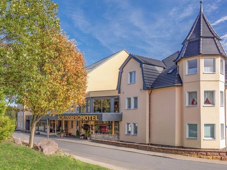 Blick auf Türmchen und Eingangsbereich des Schlossberghotel Oberhof sowie herbstliche Bäume.