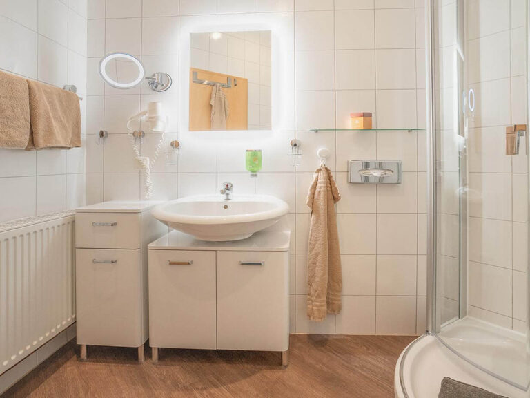 Helles Duschbad mit beleuchtetem Kosmetikspiegel und Föhn.