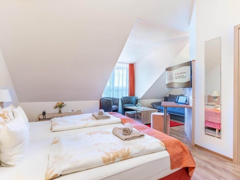 Blick ins Komfort Zimmer mit Bett, Sitzecke, Tablet und TV.