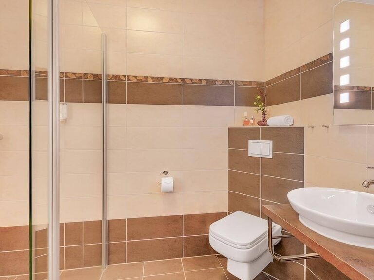 Modernes Bad in Erdtönen mit Dusche und beleuchtetem Spiegel.