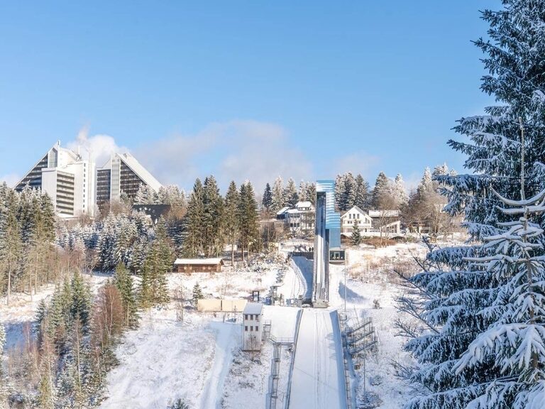 Blick vom Gegenhang zur Jugendschanze Oberhof mit Wohnhäusern und dem berühmten Panorama-Hotel im Hintergrund.